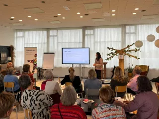 Een grote zaal met een groep mensen zittend op stoelen in theateropstelling kijkend naar de presentatie